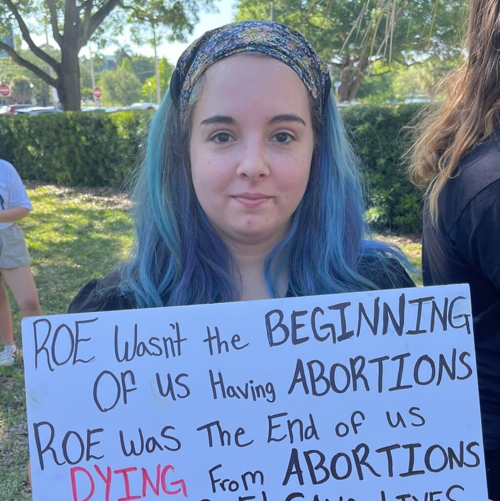 Photo of a person holding a sign reading ROE wasn't the beginning of us having abortions, roe was the end of us DYING from abortions.